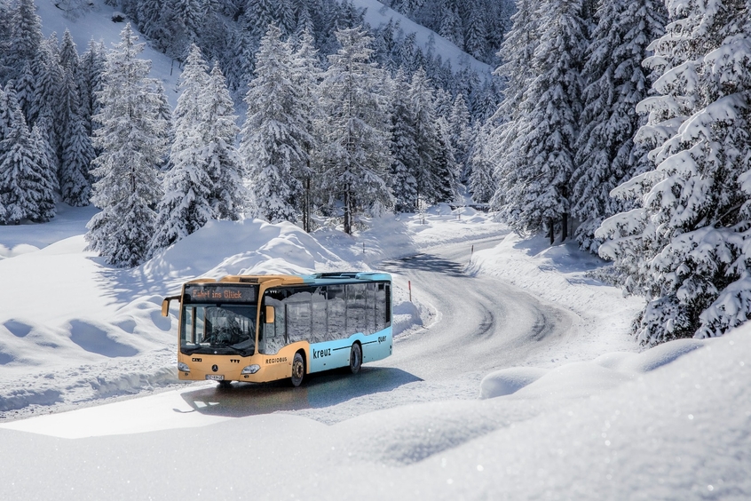 Im Bild ein Bus, der durch eine Winterlandschaft fährt.