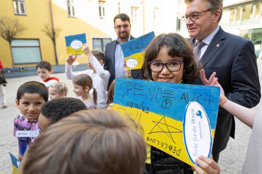 Landeshauptmann Platter mit Volksschulkindern, die eine Ukraineflagge mit persönlichen Botschaften in der Hand halten.