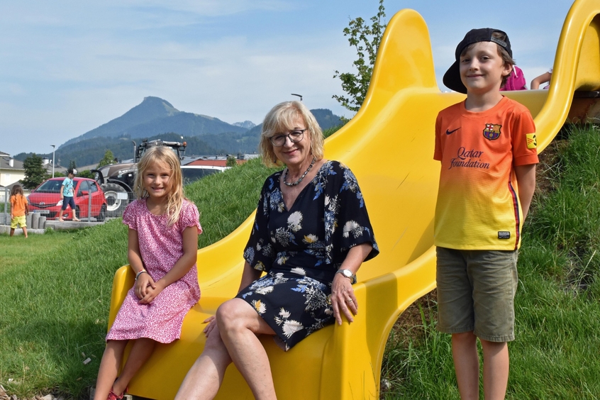 Beate Palfrader mit zwei Kindern auf gelber Rutsche auf einem Spielplatz sitzend 