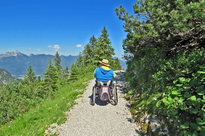 Mann in Rollstuhl auf Wanderweg; Wanderweg ist breit und nicht sehr steil