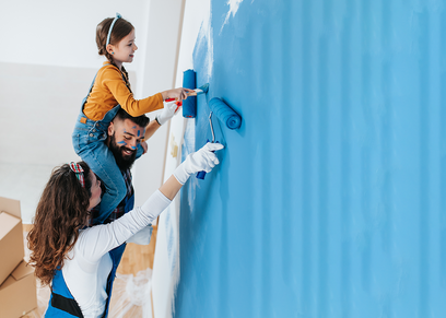 Vater, Mutter und Kind beim Streichen einer Wand in einem Wohnzimmer.